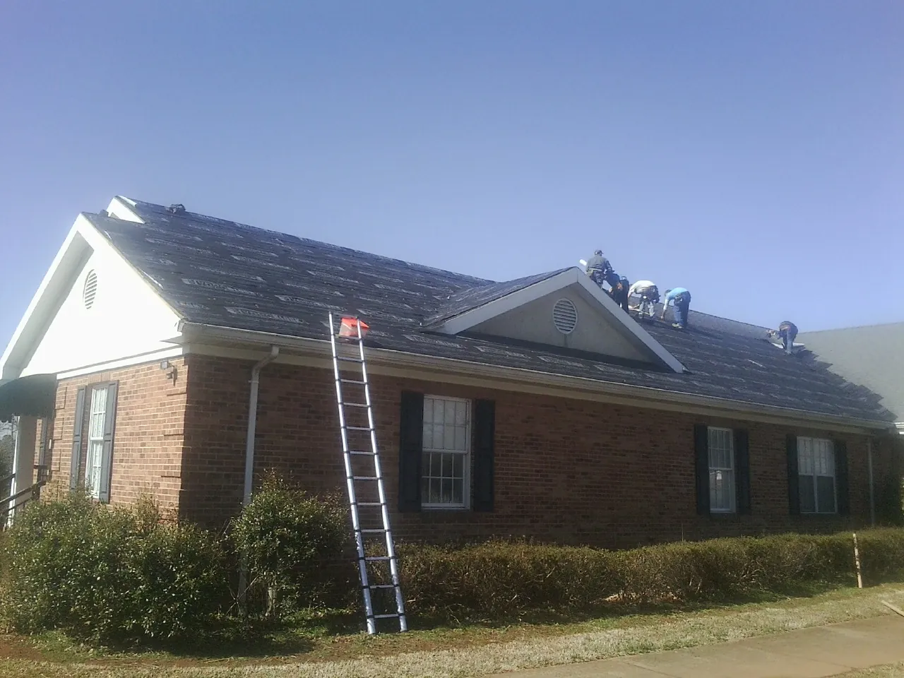 Crew tearing shingles off a brick ranch roof with a ladder set — Emergency Roof Repair work by our crew in Cunningham