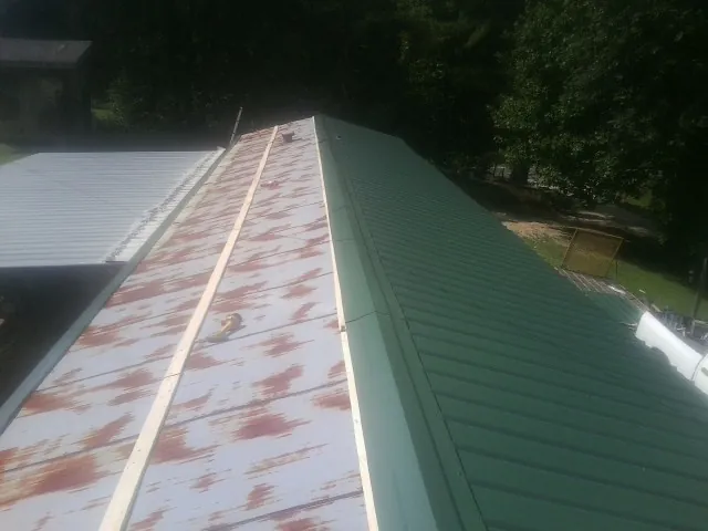 Old rusted panels beside newly installed green metal roofing — Wind Damage Roof Repair by Roofing Brothers in Cunningham
